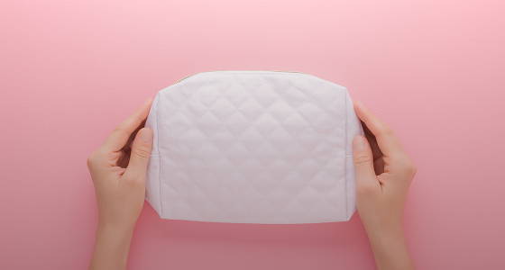 Quilted pouch held by hands, pink backdrop.
